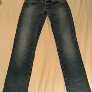 Blå dondup jeans  - Snygga blå dondup jeans med klassisk tvätt och raka ben. Jeansen har fem fickor, bälteshällor och subtila slitningar framtill. Bakfickorna har dekorativa sömmar och det finns en läderpatch vid linningen. Perfekta för en avslappnad stil. Passar dig som är under 175.