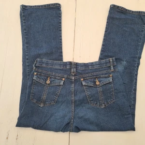 Blå bootcut jeans med fickdetaljer - Snygga blå jeans från Lee med klassisk bootcut-modell. Jeansen har fem fickor, varav bakfickorna har lock och knappdetaljer. Tillverkade i mjukt denimtyg med en bekväm passform och normal midja. Perfekta för dig som gillar en tidlös jeansstil. Utsvängd passform, meddela om du vill se dem på