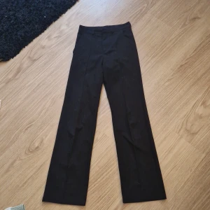 Svarta kostymbyxor från Kappahl - Svarta kostymbyxor från Kappahl i storlek 170. Byxorna har raka ben, bälteshällor och klassisk passform. Perfekta för en clean och stilren look. Materialet känns mjukt och följsamt, och färgen är helsvart.