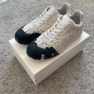 Maison Margiela Sneakers – Stl 43  - Maison Margiela Sneakers – Stl 43 👟🖤 Helt nya Maison Margiela-sneakers i vit/svart med unik målad design. Aldrig använda – endast provade hemma.  • Storlek: 43 • Skick: Helt nya ✅ • Ingår: Skor + originalkartong (lite sliten, se bild) 📦 • Dustbag ingår ej (behåller själv) • Nypris: ca 6000 kr 💸 • Snittpris på Vinted: ca 3000 kr 📊  💡 Köpt via Plick. Tidigare ägare uppgav att de är äkta och visade kvitto, men jag kan inte garantera äktheten till 100 % – därav det låga priset.