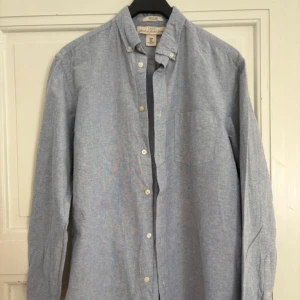 Blå skjorta från L.O.G.G. i bomull - Klassisk ljusblå skjorta från L.O.G.G. med button down-krage och bröstficka. Skjortan är i bomull, har lång ärm och stängs med vita knappar framtill. Perfekt för en clean och avslappnad stil.