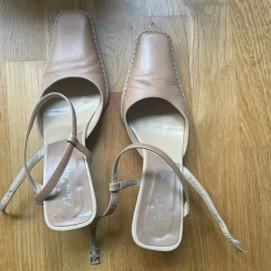 Beige klackskor med fyrkantig tå Enzo Star - Snygga beige klackskor från Enzo Star med fyrkantig tå och bred klack. Skorna har en tunn rem runt vristen med spänne och är tillverkade i skinn. Perfekta för dig som gillar stilrena och trendiga detaljer.