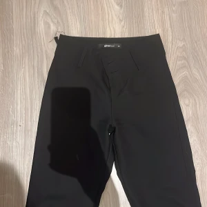 Svarta kostymbyxor från Gina Tricot XS - Svarta kostymbyxor från Gina Tricot i storlek XS. Byxorna har raka ben, hällor för bälte, fickor fram och bak med knappdetaljer. Snygg och stilren modell som passar perfekt till en dressad look. använda ett par gånger. köpte dom för 600