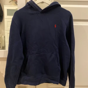 Marinblå hoodie från Polo Ralph Lauren - marinblå hoodie från Polo Ralph Lauren med klassisk röd logga broderad på bröstet. Köptes ny på Kids Brand Store för 1000kr. XL i ”barnstorlek” så skulle säga att S och även M funkar. Använd en del men fortfarande bra skick. Köparen står för frakt!