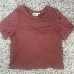 Roströd topp med broderade ärmar Kappahl - Superfin roströd topp från Kappahl med korta ärmar i broderad bomull och snygga håldetaljer. Toppen har en rund halsringning och är i mjukt material, perfekt för en chill och trendig look.