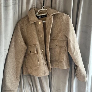 Beige overshirt från Zara i ullmix - Snygg beige overshirt från Zara i ullmix med stora fickor framtill och guldiga tryckknappar. Jackan har klassisk krage, raka ärmar och en croppad passform som ger en trendig look. Jackan är knappt använd och inga tecken på användning. Hör av dig vid frågor!💗
