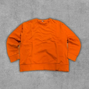 Orange sweatshirt i bomull - En enkel och stilren orange sweatshirt med rund hals och långa ärmar. Tröjan har breda muddar vid ärmslut och nederkant, vilket ger en avslappnad och trendig look. Perfekt för dig som gillar färg och vill sticka ut lite extra.