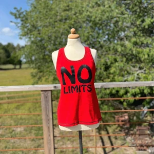 Röd linnetopp NO LIMITS från Oxide - Röd ärmlös linnetopp från Oxide med svart text 'NO LIMITS' framtill. Modellen har brottarrygg och svarta kontrastsömmar som ger en sportig vibe. 