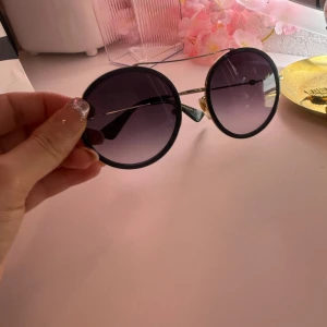 Runda solglasögon från Gucci det är utsn lådor  - Snygga runda solglasögon från Gucci med svarta bågar och tunna guldfärgade metallskalmar. Glasen är mörktonade och ger en cool retrovibe. Perfekta för dig som vill sticka ut med en statement-accessoar.det är utan lådor 