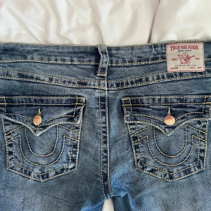 True religion jeans low waist - Säljer ett par blå True Religion Joey jeans med låg midja och flare-ben. Klassiska stora fickor med guldiga knappar. Logga bak och snygg tvättad denim. Slitna ner till benen då dom är för långa, men annars inga defekter. Köpte för runt 1300kr🩷