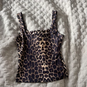 Leopardmönstrad linnetopp med breda axelband - Säljer en snygg leopardmönstrad linnetopp med breda axelband och rak halsringning. Toppen har en figurnära passform och är tillverkad i ett stretchigt syntetmaterial. Perfekt för dig som vill sticka ut med ett djurmönster i brunt och svart.