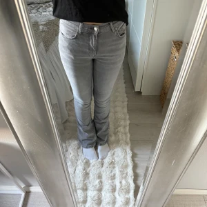 Grå bootcut jeans från Gina Tricot - Säljer ett par grå jeans från Gina Tricot i modellen bootcut. Jeansen har klassisk femficksdesign, normal passform och är tillverkade i mjukt denimtyg. Snyggt ljusgrå färg som passar till det mesta och stängs med dragkedja och knapp.