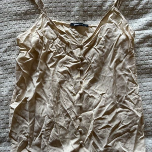Beige linnetopp från Gina Tricot - Snygg beige linnetopp från Gina Tricot med knappar framtill. Toppen har smala axelband och en v-ringad design, perfekt för varma dagar.