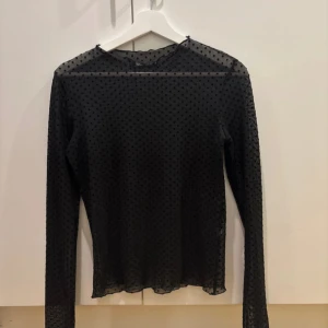 Svart meshblus med prickar Gina Tricot - Svart transparent meshblus med polkadots från Gina Tricot i storlek XS. Blusen har lång ärm och är täckt av små svarta prickar för en trendig look. Perfekt att styla lager på lager eller med ett snyggt linne under.