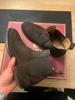 Bruno Magli chelsea boots - Säljer ett par stilrena mörkbruna chelsea boots från Bruno Magli i mjuk mocka. Skorna har elastiska paneler på sidorna, rund tå och klassisk platt sula. Insidan är fodrad i ljust skinn för extra komfort. Perfekta för dig som vill ha en clean och tidlös look. Gjorda i Italien och topp kvalitet. Köpta för ca 4500kr och sulan är ändrad till gummi för att vara mer hållbar hos en skomakare för 700kr.