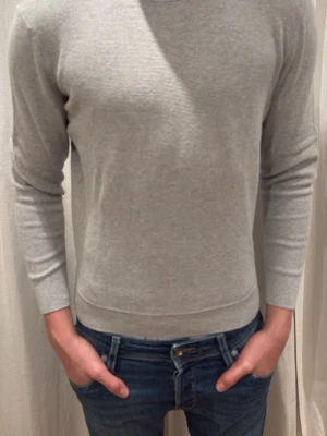 Ljusgrå stickad tröja - Säljer en stilren ljusgrå stickad tröja med rund hals och långa ärmar. Tröjan har en tight passform och är tillverkad i mjukt material som känns skönt mot huden. Perfekt att matcha med jeans för en clean look. Något typ av reflat material från Zara, storlek S