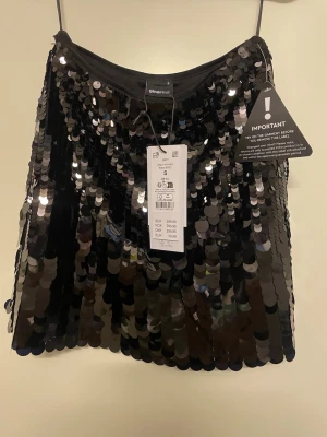 Ny oanvänd Svart paljettkjol från Gina Tricot - Ny oanvänd svart paljett kortkjol från Gina Tricot i storlek S/36.