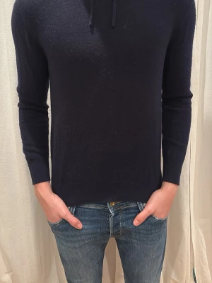 Mörkblå hoodie i kashmir - Säljer en stilren mörkblå hoodie i mjuk kashmir. Tröjan har huva med snörning och långa ärmar. Passformen är normal och materialet känns riktigt lyxigt och skönt mot huden. Perfekt för dig som vill ha en enkel men snygg hoodie. Från sayles och storlek xs