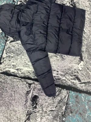 Svart pufferjacka från Polo Ralph Lauren - Säljer en svart pufferjacka från Polo Ralph Lauren med huva och dragkedjor. Jackan har det klassiska röda Polo-logot på bröstet och flera praktiska fickor med dragkedja. Perfekt för kalla dagar och riktigt snygg till streetwear-stilen.