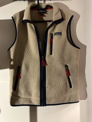 Beige fleeceväst från Patagonia XS - Patagonia väst, väldigt bra skick. Snygg inför våren, den är beige med blåa detaljer alltså en väldigt svår färg att hitta på nätet🤩 hör av er vid minsta lilla fundering