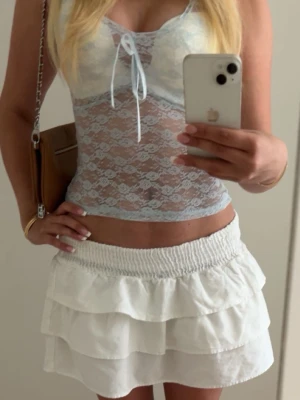 Ljusblå spetsig linnetopp med knyt - Säljer en ljusblå, transparent linnetopp i spets med söt knytning framtill. Toppen är croppad och har tunna axelband. Perfekt för varma dagar och ger en romantisk vibe till din outfit.