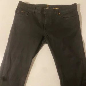 Boss byxor  - Säljer ett par svarta BOSS Delaware jeans i slim fit. Klassisk femficksmodell med snygga orangea detaljer och logga på fickan och bak. Jeansen är i ett mjukt bomullsmaterial med lite stretch för extra komfort. Perfekta för dig som gillar en smalare passform.