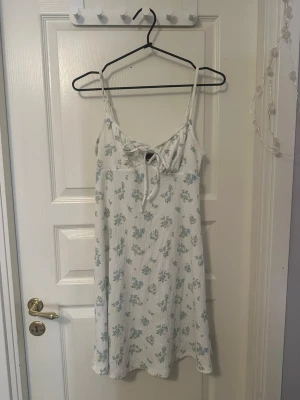 Blommig sommarklänning Gina Tricot XS - Supersöt vit kortklänning från Gina Tricot med blått och grönt blommönster. Klänningen har smala axelband och snören man kan knyta där fram😽💋