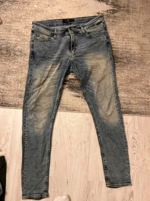 Blå skinny jeans från Zara Man - Säljer ett par blå skinny jeans från Zara Man Denim Collection. Jeansen har slitna detaljer och ljusa partier framtill och baktill för en cool, använd look. Klassisk femficksmodell med dragkedjegylf och smal passform hela vägen ner.