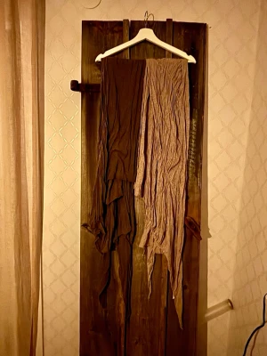 Brun och beige randiga sjalar - Unika sjalar från Melmelli, i två färger, ena sjalen är brun och andra sjalen beige med tunna ränder. Sjalarna har ett långt, asymmetriskt fall och är gjorda i mjuk, tunn 100% bomull som ger en avslappnad vibe. Perfekt för dig som vill sticka ut med lager på lager. Sista bilden är exempelbild, ej bild på dessa sjalar.