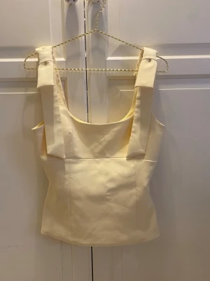 Ljusgul topp med rosettband - Säljer en ljusgul topp med breda axelband och rosetter på axlarna. 