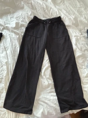 Svarta mjukisbyxor med snörning - Svarta mjukisbyxor med breda ben och resår i midjan. Byxorna har snörning och stora fickor framtill. Perfekta för chill dagar eller när du vill ha det extra bekvämt. Storlek är 150