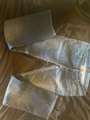 Blå bootcut jeans från Crocker W32 L34 - Säljer ett par klassiska blå jeans från Crocker, modell CR-324. De har bootcut passform, fem fickor och snygga slitningar för en avslappnad look. Jeansen är tillverkade i tåligt denimtyg och har detaljerade sömmar på bakfickorna.