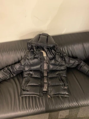 Svart Moncler pufferjacka - Säljer en svart pufferjacka från Moncler med stor huva och två dragkedjeförsedda fickor. 