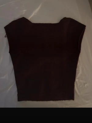  stickad topp från Nelly - Mysig brun stickad topp från Nelly i storlek XS. Toppen har en croppad passform och är ärmlös med breda axlar. Perfekt att styla med höga jeans eller kjol för en trendig look.