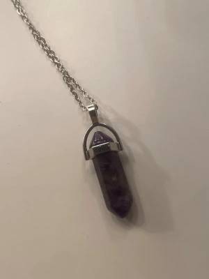 Lila kristallhalsband med silverkedja - Säljer ett halsband med en spetsig lila kristall i silverfärgat fäste och kedja. Kristallen har en cool, naturlig marmorering och kedjan är i metall med karbinlås. Det är en äkta ametist kristall som är ljusare i verkligheten än på bild. Helt oanvänd! 🫶