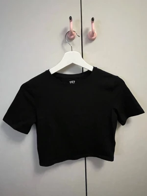Svart croppad topp från lager 157 - En enkel och stilren svart croppad topp från lager 157. Toppen har rund halsringning och korta ärmar. Materialet är strechigt . Oanvänd.