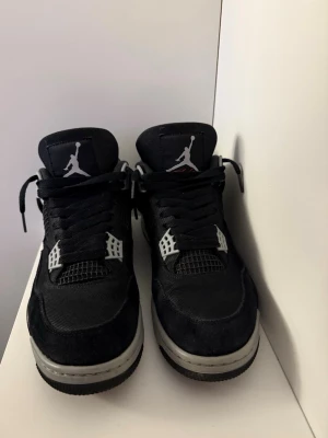 Nike Air Jordan 4 Retro svart/grå - Säljer ett par Nike Air Jordan 4 Retro i svart med grå och vita detaljer. Skorna har klassisk mesh och mocka på ovandelen, Jumpman-logga på plös och häl samt snörning. Snygg siluett med platt sula och ikoniska plastdetaljer vid snörningen.