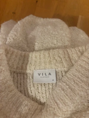 Beige stickad tröja från VILA - Mysig beige stickad tröja från VILA med rund hals och långärmad passform. Tröjan har en enkel, clean look och är perfekt för lager på lager under kyliga dagar. Materialet är mjukt och ger en avslappnad vibe.