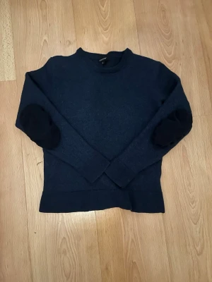 Mörkblå stickad tröja Paul & Friends - Mörkblå stickad tröja från Paul & Friends i storlek L för barn asså ungefär 12 år fast har krympt mycket så den är ungefär storlek 8-9 år. Tröjan har rund halsringning, långa ärmar och svarta armbågslappar som ger en snygg detalj. Perfekt för kyliga dagar och enkel att matcha med jeans eller chinos.