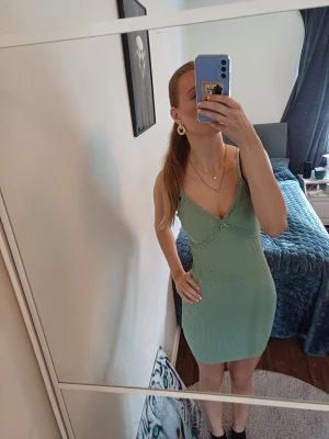 Grön ribbad kortklänning med spets - Supersöt ljusgrön kortklänning med smala axelband och v-ringning. Klänningen är ribbad och har fina spetsdetaljer längs urringningen samt en liten rosett framtill. Perfekt för sommarens alla tillfällen! ❤️