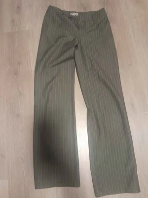 Randiga kostymbyxor  - Snygga kostymbyxor i mörkgrått med tunna vita ränder. Byxorna har en rak och lite vidare passform med klassisk midja. Perfekta för en clean och stilren look.