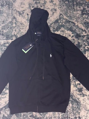 Ralph Lauren Hoodie - Svart Ralph Lauren hoodie i klassisk och tidlös design. Mjuk och bekväm med bra passform, perfekt för både vardag och en clean street/old money-look.