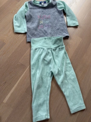 Lupilu i set strl 74/80 Grå och mintgrön babytröja - Söt långärmad tröja för baby i grått och mintgrönt med texten 'I believe in unicorns' broderad framtill. Tröjan har mjuka ärmar och rund hals. Perfekt för förskolan 