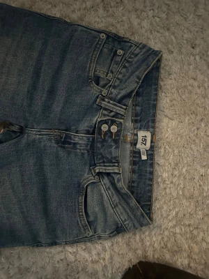 Blå bootcut jeans från 157 - Säljer ett par klassiska blå bootcut jeans från 157 med normal passform. Jeansen har fem fickor, dubbla knappar i midjan och snygga kontrastsömmar. Tillverkade i slitstarkt denimtyg som ger en tidlös look. Strl. Xs/S, endast använda en gång.