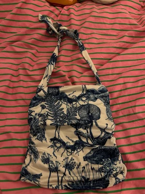  linnetopp med knyt/Lniany top z krawatem - Säljer en beige linnetopp med marinblå botaniskt mönster. Toppen har knyt i nacken och är ärmlös, med en tight passform. Materialet känns mjukt och stretchigt, Perfekt för varma dagar och har en unik, naturinspirerad look🪽