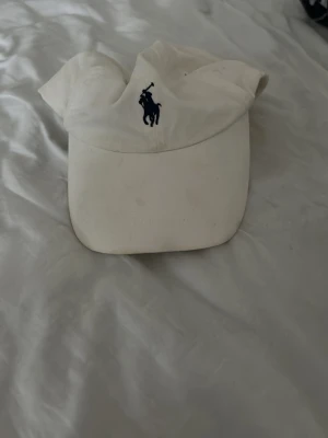 Vit keps från Polo Ralph Lauren - Säljer en klassisk vit keps från Polo Ralph Lauren med den ikoniska polospelaren broderad framtill och POLO-text baktill. Fleck på insidan annars inga problem 