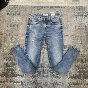 Blå skinny jeans från FSBN - Snygga blå skinny jeans från FSBN med slitningar och tvättad look. Klassisk femficksmodell med knapp och dragkedja. Jeansen har smal passform och är tillverkade i jeansmaterial med ljusa partier och detaljerade sömmar.