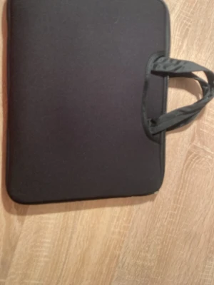 Svart datorväska med handtag - En stilren svart datorväska med mjukt material och praktiska handtag. Väskan har en enkel, clean look utan synliga loggor eller mönster. Perfekt för att bära din laptop till skolan eller jobbet.