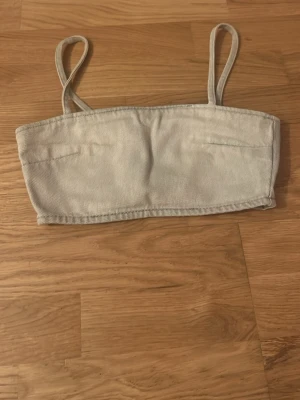 Grå bandeau topp med smala band - Säljer en enkel och stilren bandeau topp i grått med smala axelband. Toppen har en rak skärning och är sydd i ett mjukt bomullsliknande material. Perfekt för varma dagar eller som layering piece.