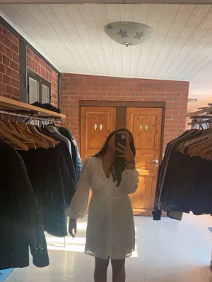 Vit kortklänning från Bubbleroom - Supersöt vit kortklänning från Bubbleroom med broderade blommor, v-ringning och knappar framtill. Klänningen har långa ärmar och markerad midja med smock baktill. Perfekt för sommarens alla tillfällen!💕💕